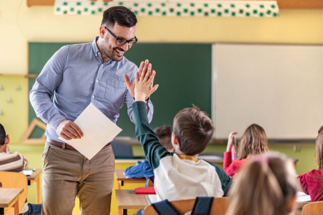 Happy Teacher And Schoolboy Giving Each Other High Five On A Class.